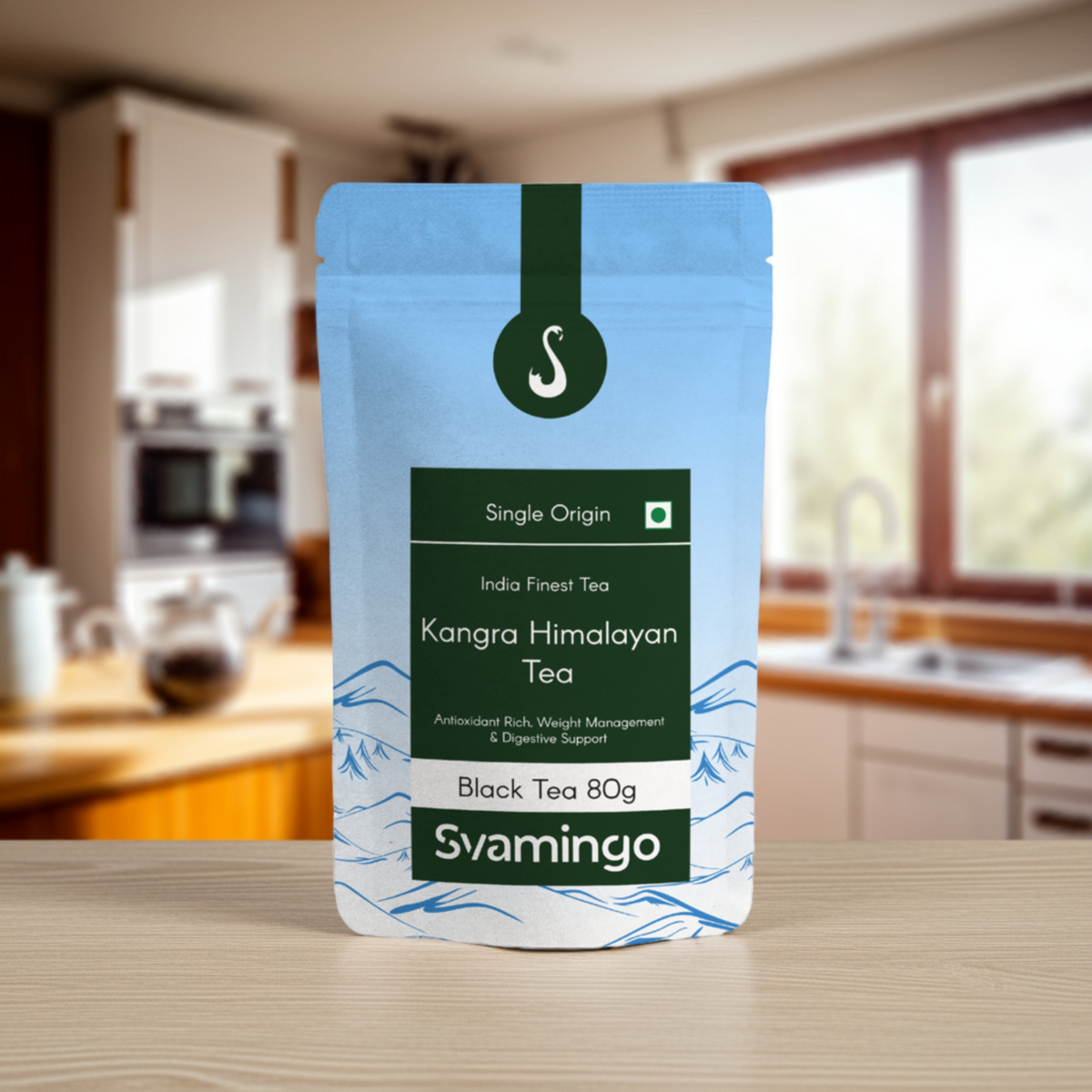 Svamingo kangra first flush black tea pouch 80g on a wooden counter in kitchen with tea pot, utensils in background