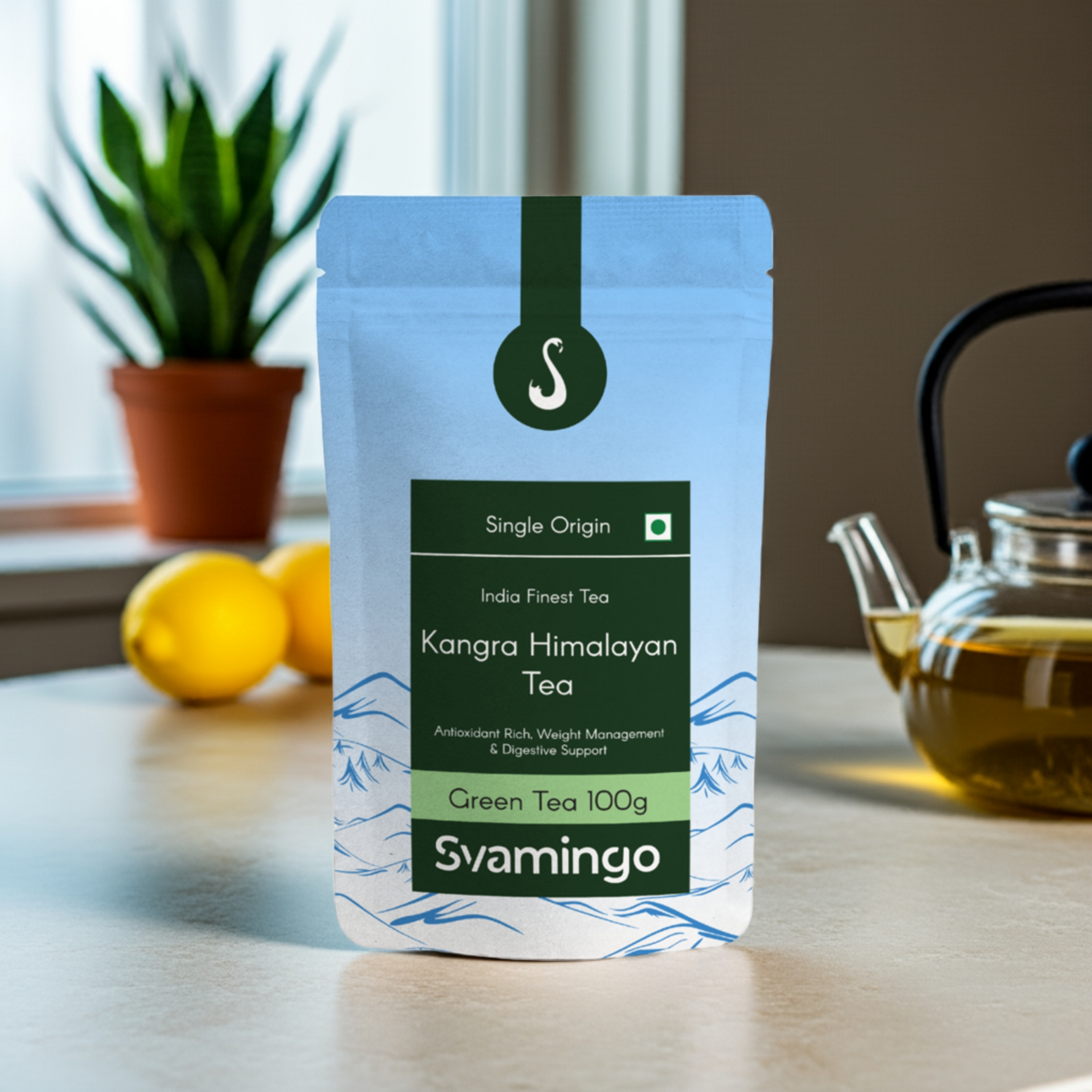 Svamingo kangra himalayan green tea pouch 100g on a marble counter in kitchen with lemons, plants and green tea pot in the background